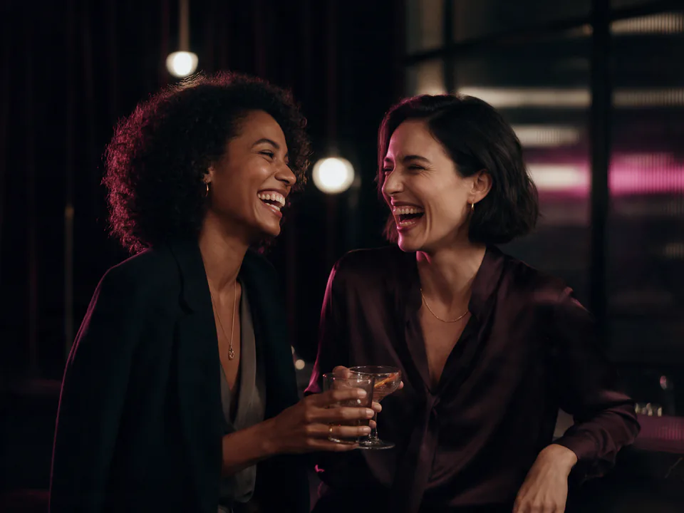Duas mulheres conversam e riem em um ambiente noturno.